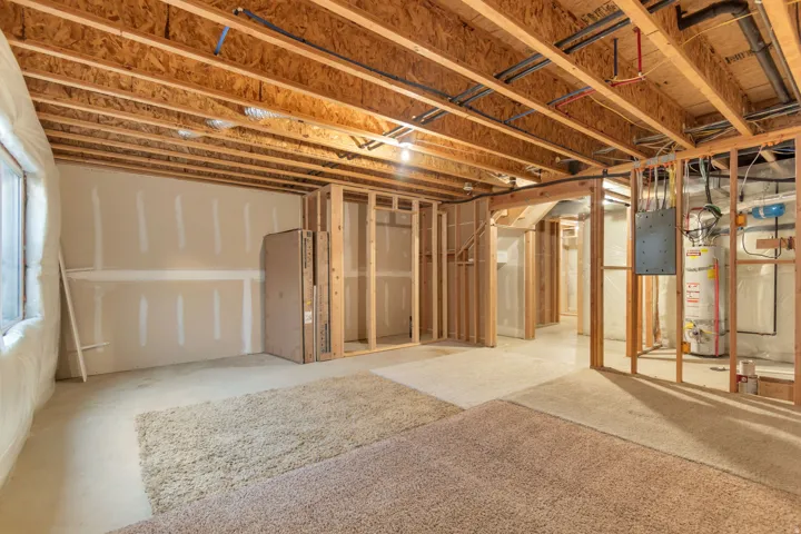 Unfinished basement featuring exposed wood joists, framed walls, Bathroom plumbing, and a large window