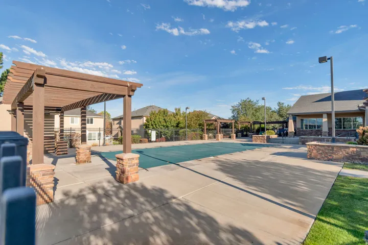 Community Pool.  Two wood pergolas with stone-clad bases, a pool with a cover, and a clubhouse with stone accents