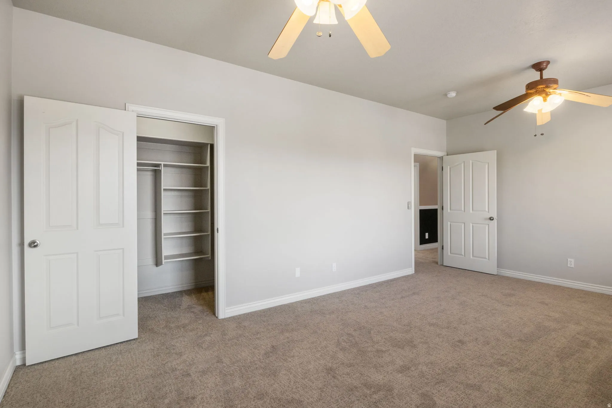 Carpeted room with light gray walls, white trim, and two ceiling fans with light fixtures