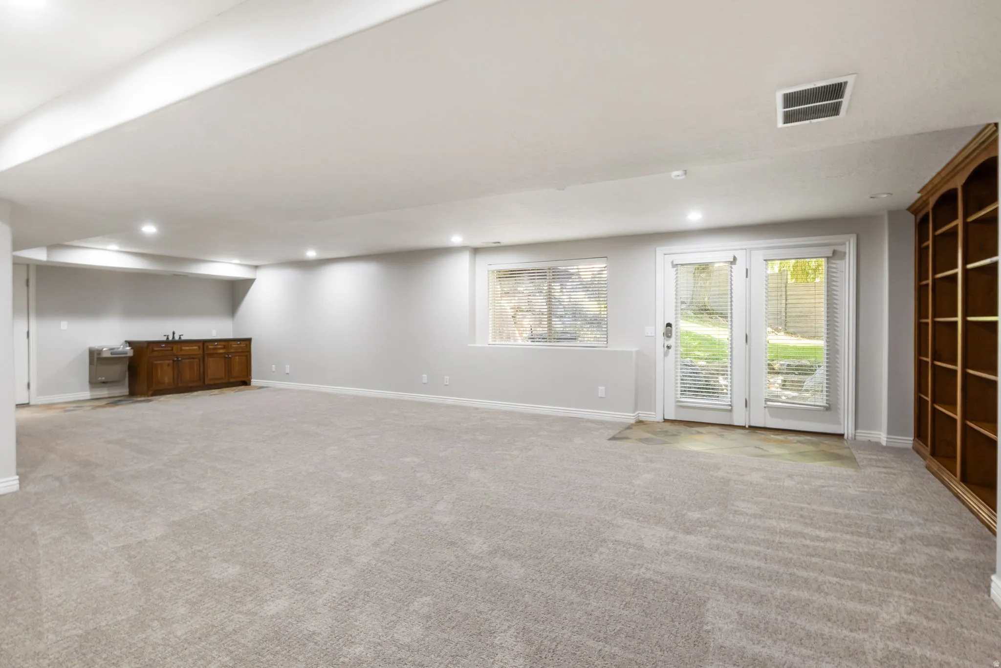 Spacious room featuring light-colored carpeting, recessed lighting, and a built-in wet bar with wood cabinetry