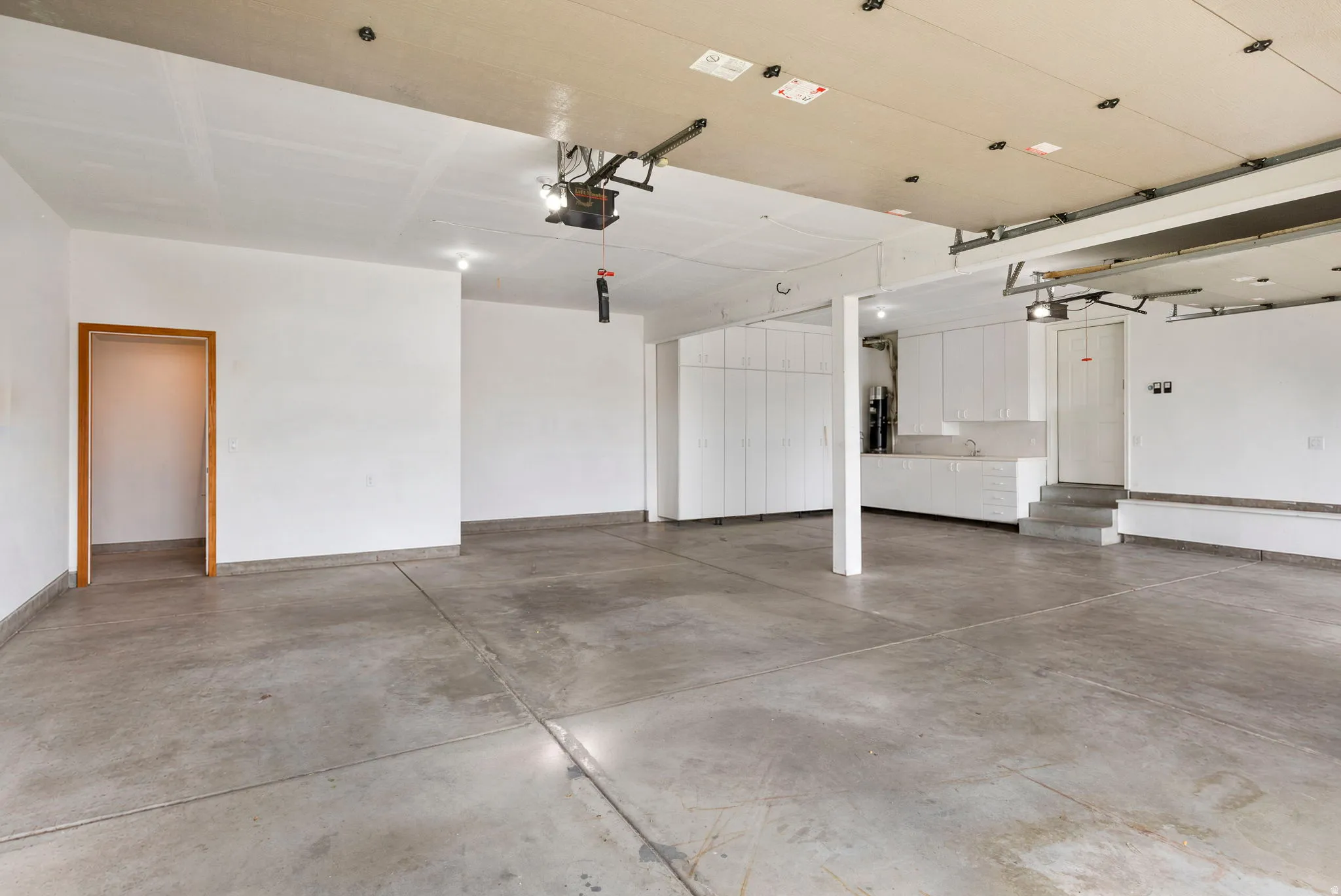 Expansive concrete floor garage with white cabinetry, overhead lighting, and an integrated garage door opener system