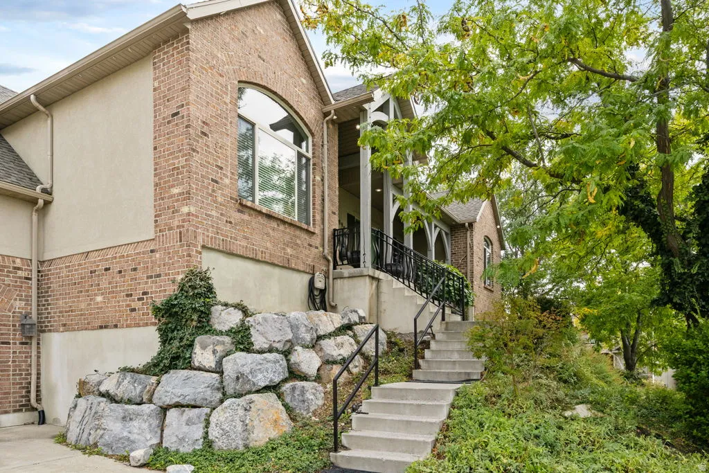Brick and stucco exterior with an arched window, rock retaining wall, concrete steps, and black metal railings