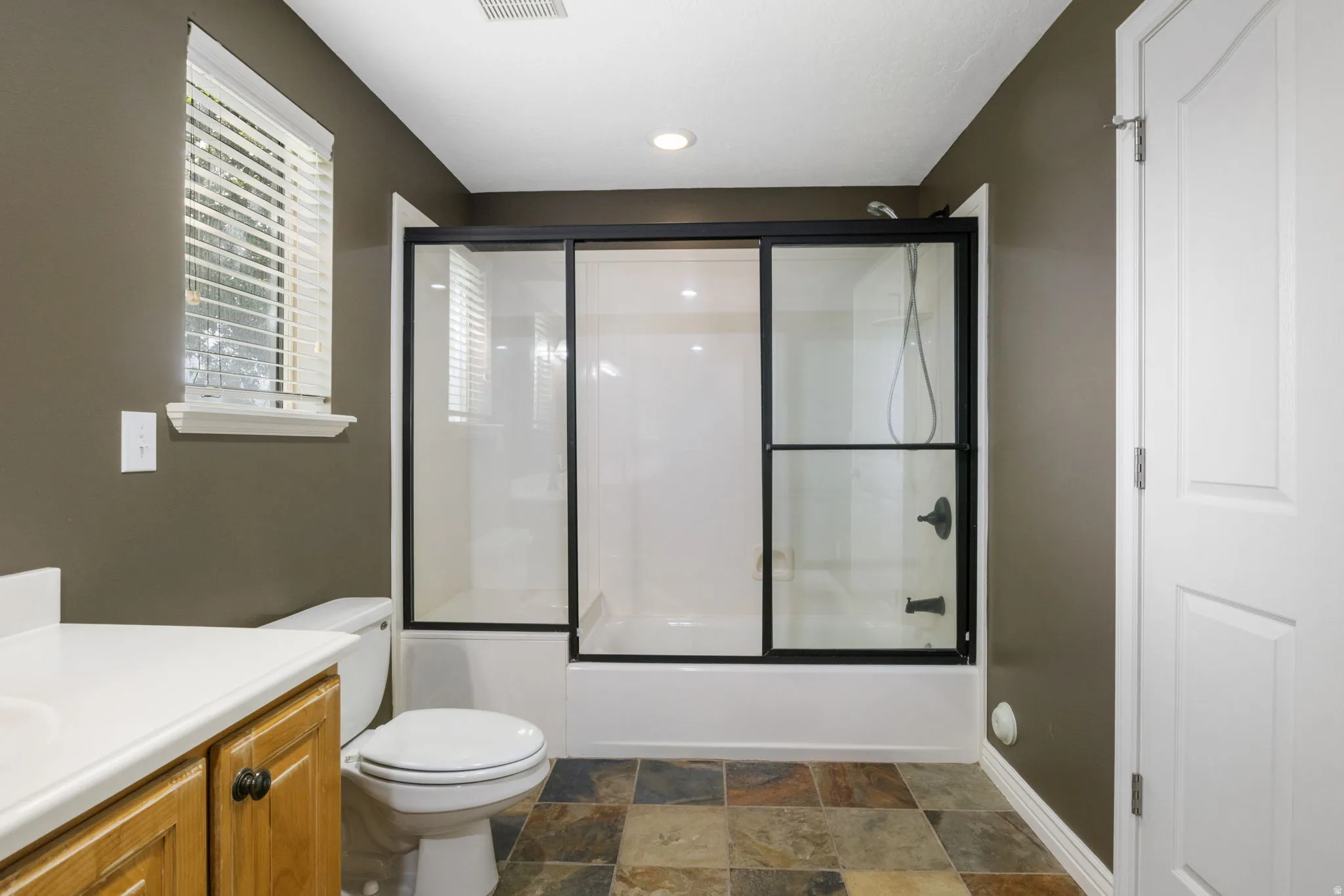 Bathroom featuring a shower-tub combination with sliding glass doors, a vanity with wood cabinetry, and multi-toned floor tiles