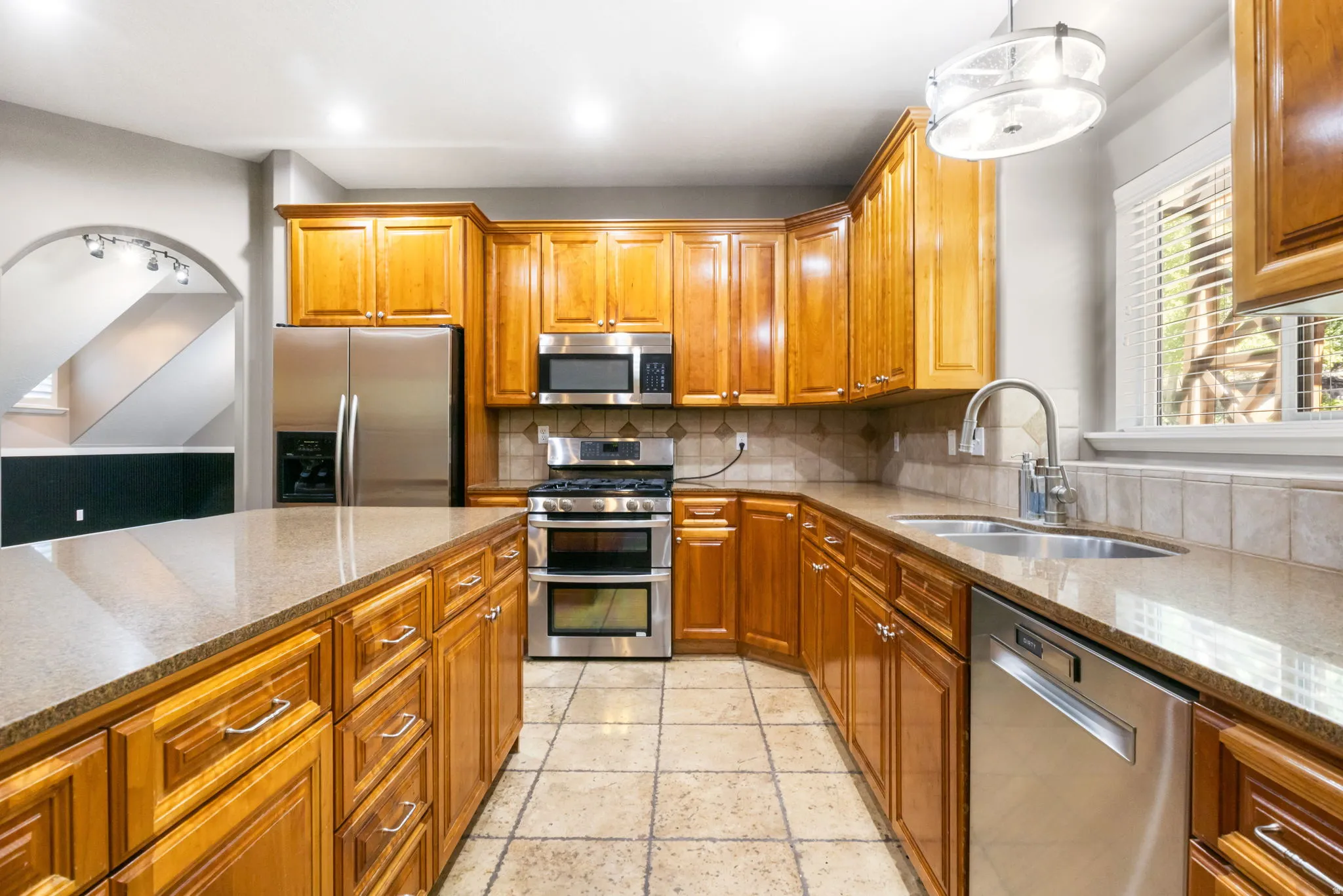 Kitchen featuring wood cabinetry, stainless steel appliances, tile flooring, and stone countertops