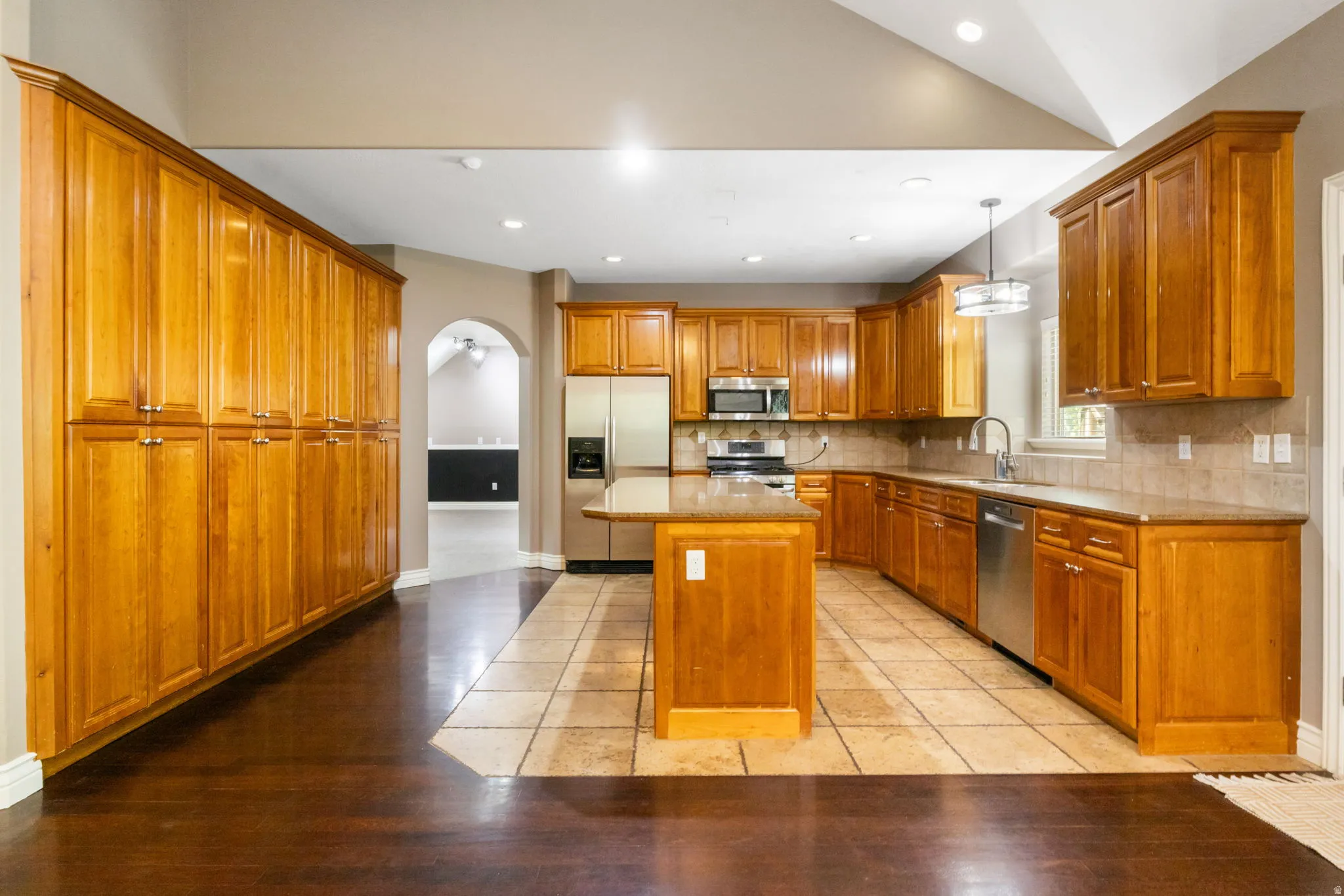 Expansive kitchen featuring wood-finish cabinetry, stainless steel appliances, a center island, and tile flooring
