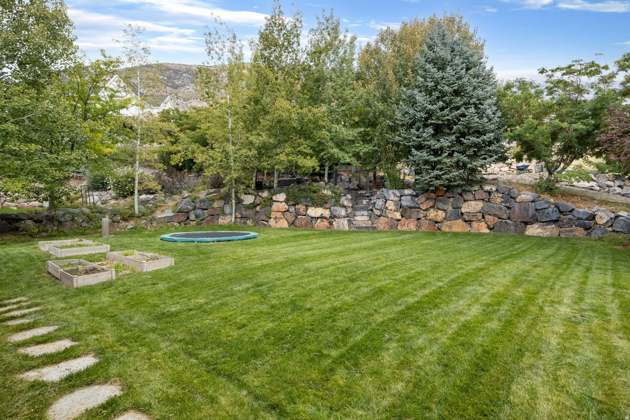 Expansive green lawn with a natural stone retaining wall, mature trees, and raised garden beds