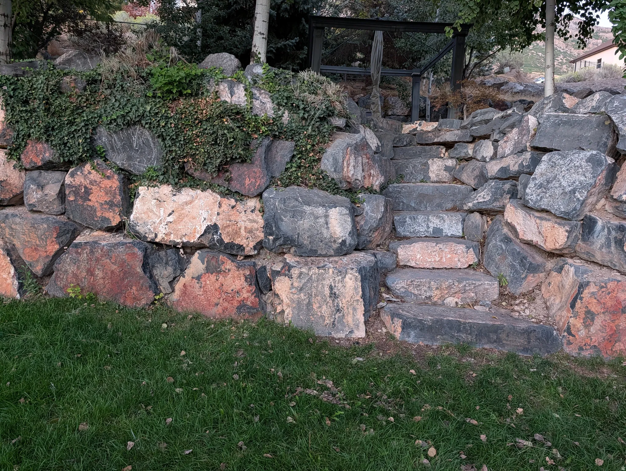 Stone retaining wall with integrated stone steps, lush ground cover, and a manicured lawn