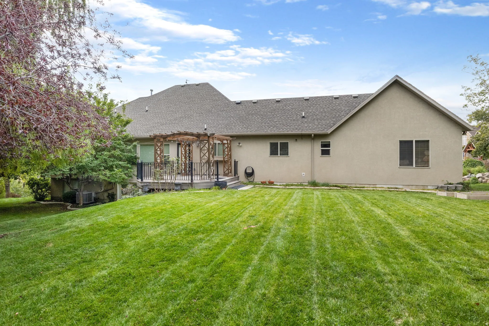 Exterior featuring stucco siding, a multi-level deck with a wooden pergola, and a spacious lawn