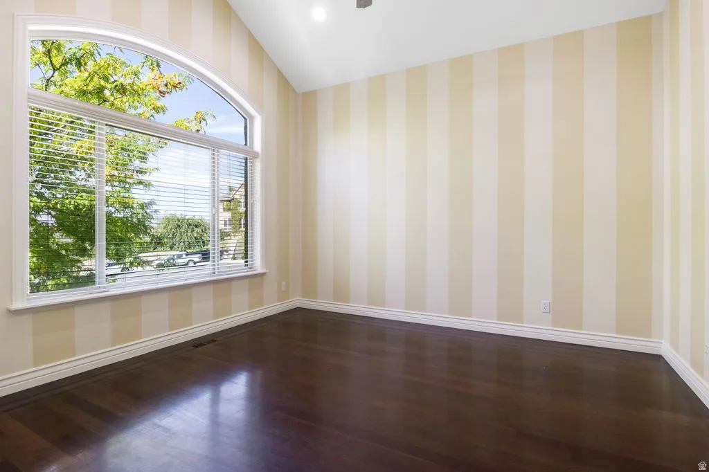 Arched window with venetian blinds, wood-finish flooring, vaulted ceiling, recessed lighting, and striped wall covering