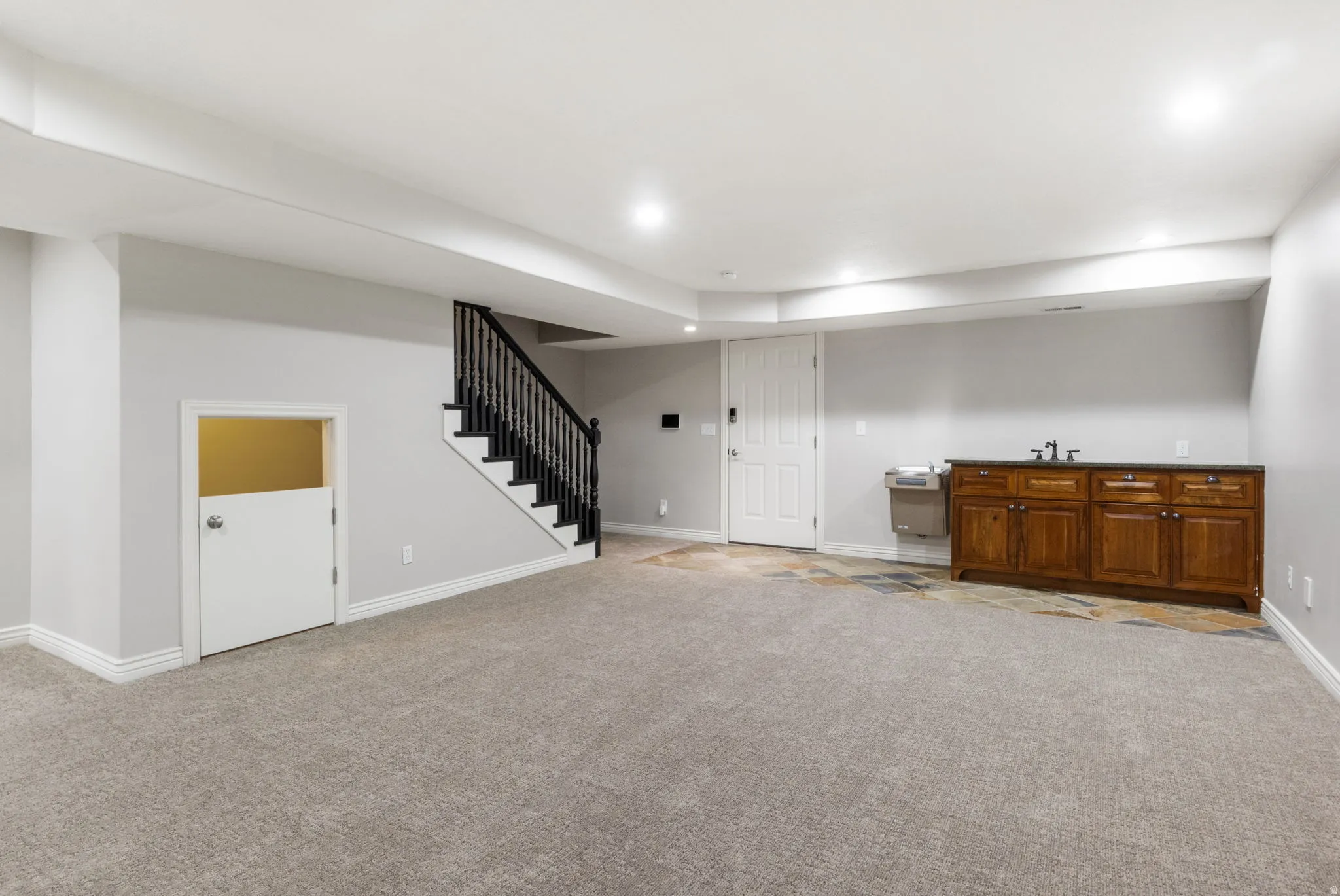 Expansive room featuring carpet flooring, built-in wet bar with wood cabinetry, and a staircase with black railings