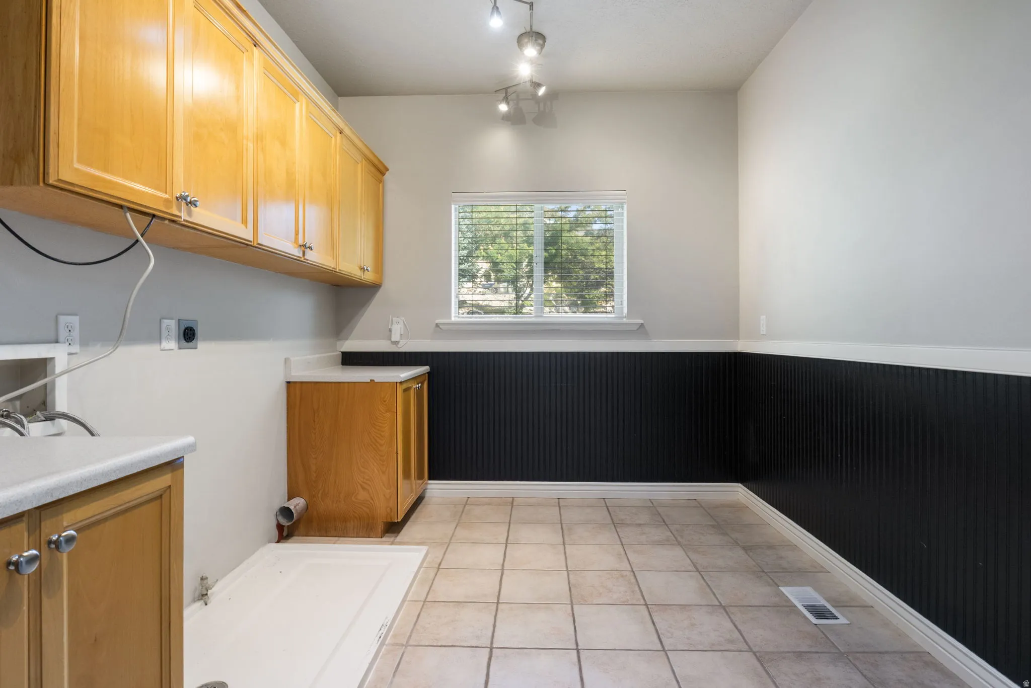 Extensive cabinetry, tile flooring, track lighting, a window with blinds, and contrasting wall paneling