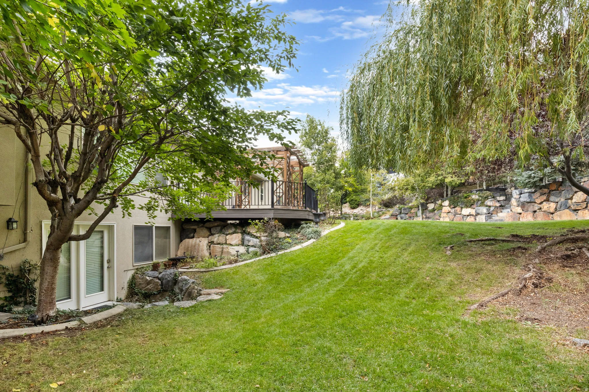 Expansive sloped lawn with mature trees and a stone retaining wall