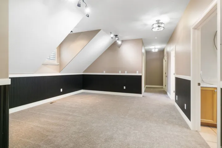 Carpeted interior space with track lighting, beadboard wainscoting, and recessed window
