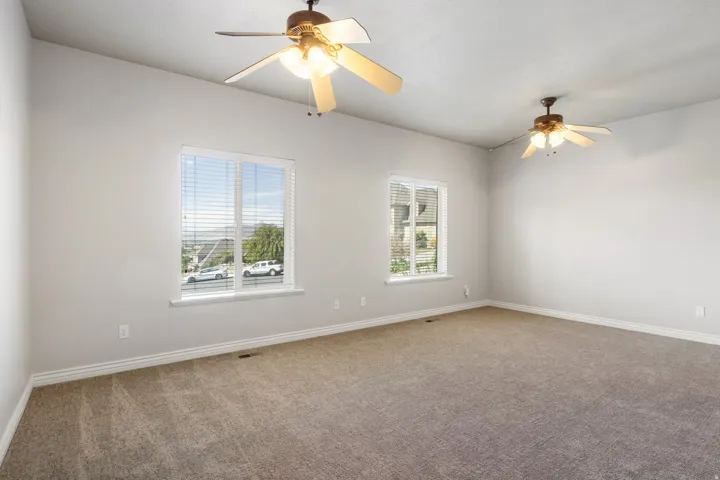 Spacious room with sloped ceilings, two ceiling fans with integrated lighting, two windows with blinds, and neutral carpeting