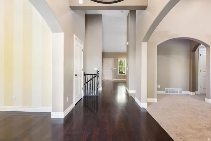 Arched doorways, dark wood-finish flooring, light carpeting, white trim, and a prominent staircase with dark balusters