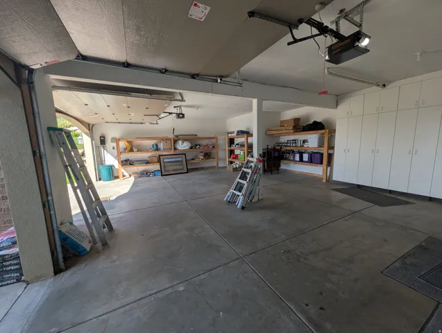 Two-car garage featuring a concrete floor, built-in cabinetry, and open shelving