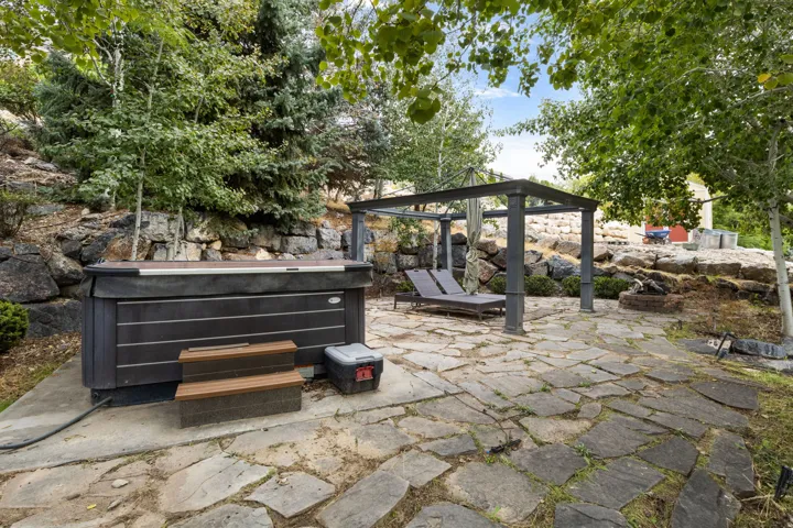 Outdoor patio featuring a hot tub, stone paving, and a metal pergola structure