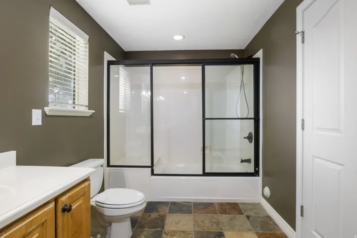 Bathroom featuring a shower-tub combination with sliding glass doors, a vanity with wood cabinetry, and multi-toned floor tiles