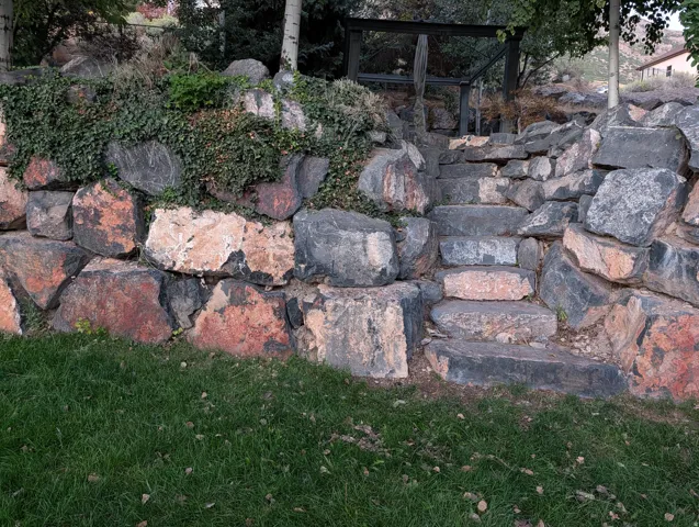 Stone retaining wall with integrated stone steps, lush ground cover, and a manicured lawn