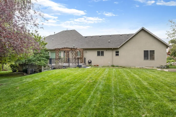 Exterior featuring stucco siding, a multi-level deck with a wooden pergola, and a spacious lawn