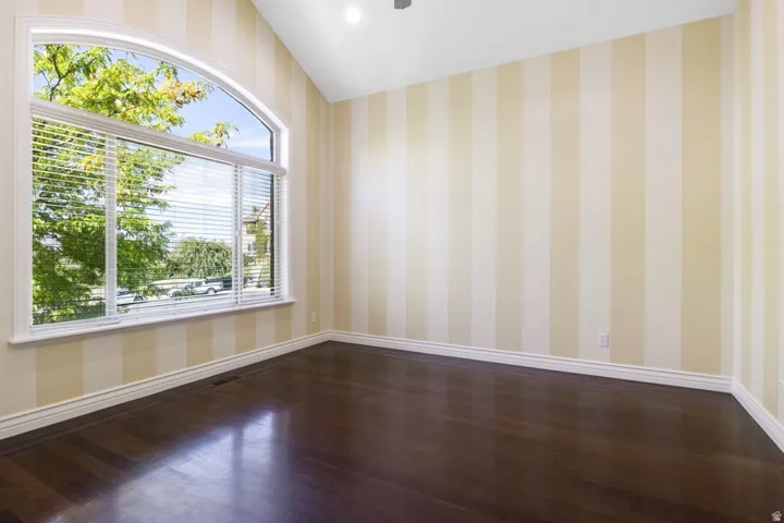 Arched window with venetian blinds, wood-finish flooring, vaulted ceiling, recessed lighting, and striped wall covering