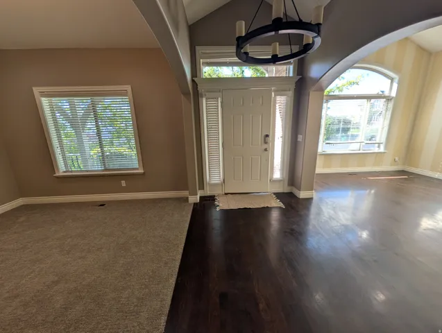 Wood-finish flooring at entry, vaulted ceiling, arched doorway, and a large window with blinds