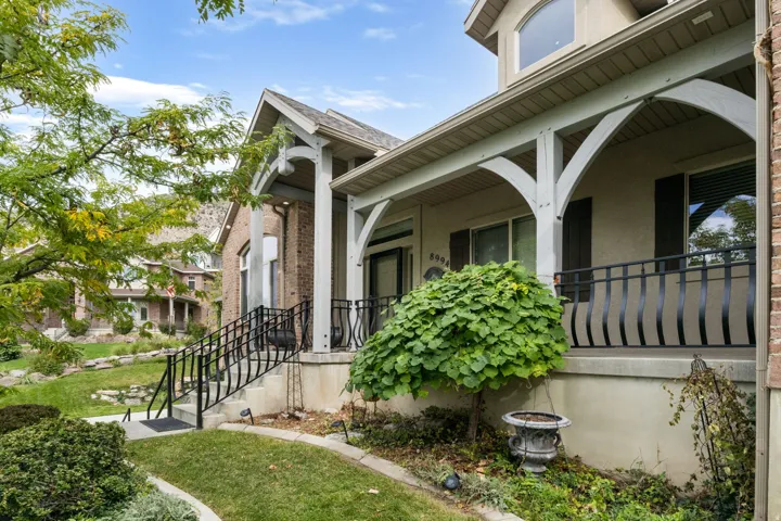 Front exterior featuring a covered porch, arched beam supports, black wrought-iron railings, brick facade, and landscaping