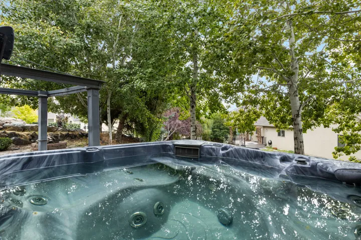 Integrated hot tub with dark finish, surrounded by mature trees and a metal pergola