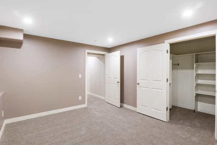 Recessed lighting, neutral wall paint, light-colored carpeting, white trim, and a closet with shelving and hanging rod