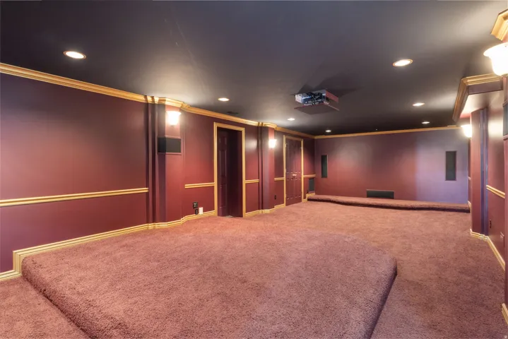 Wall-to-wall carpeting with tiered platforms, recessed ceiling lighting, wall sconces, integrated speakers, and a ceiling-mounted projector