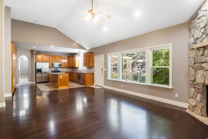 Vaulted ceiling, dark wood-finish flooring, kitchen island, stainless steel appliances, and a stone-faced fireplace