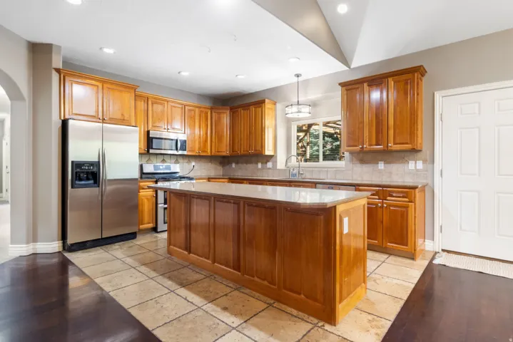 Spacious kitchen featuring a central island, wood cabinetry, stainless steel appliances, and tiled flooring