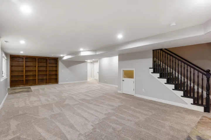 Spacious lower level featuring built-in wood shelving, recessed lighting, and a carpeted floor