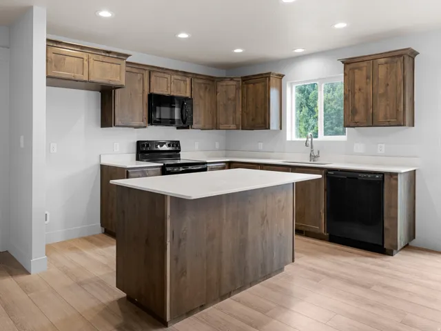 Kitchen featuring wood-finish cabinetry, light-toned countertops, a central island, recessed lighting, and integrated black appliances