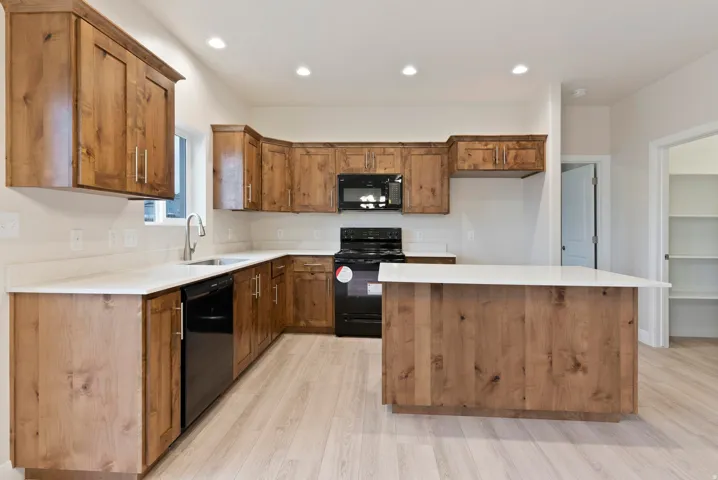 Open-concept kitchen featuring wood-finish cabinetry, light-toned countertops, a central island, and black appliances