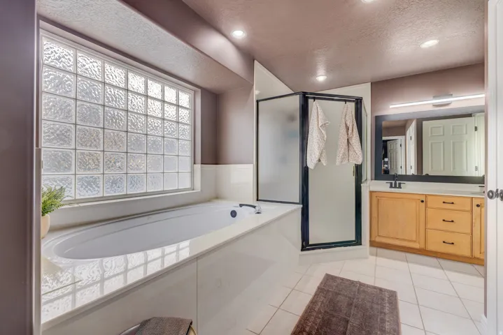 Built-in soaking tub with a tiled surround, glass block window, and adjacent enclosed shower