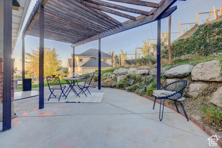 Expansive concrete patio featuring a wood pergola, brick accents, and a tiered rock retaining wall with established plantings