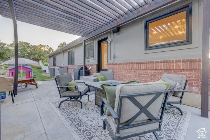 Expansive concrete patio featuring a louvered pergola, brick and stucco exterior, and black-framed windows