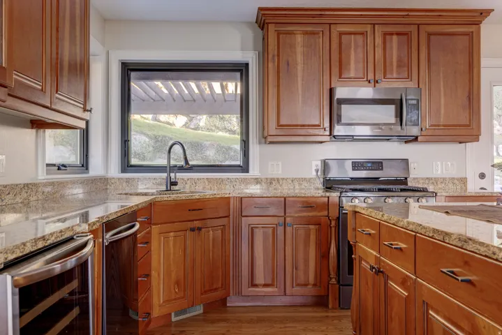 Wood-finish cabinetry, granite countertops, stainless steel appliances, corner sink with a gooseneck faucet, and a built-in beverage cooler