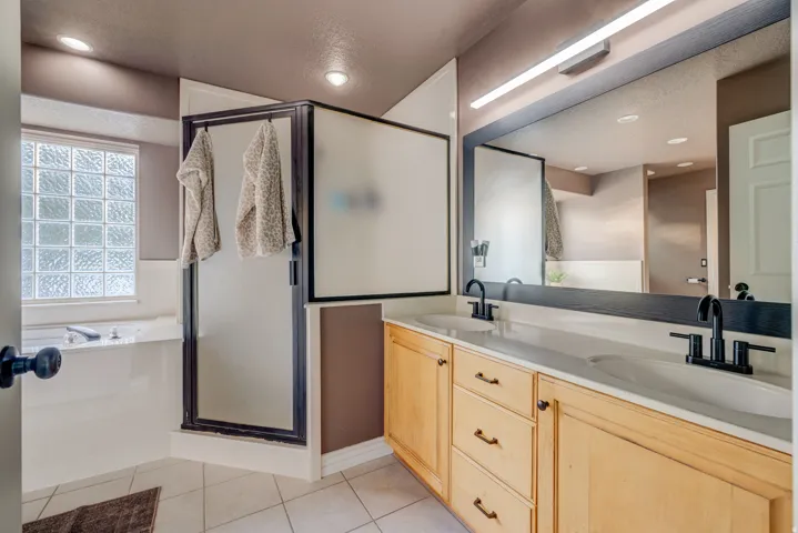 Dual vanity with integrated sinks and matte black fixtures, full-width mirror, light wood-finish cabinetry, tile flooring, and a glass block window