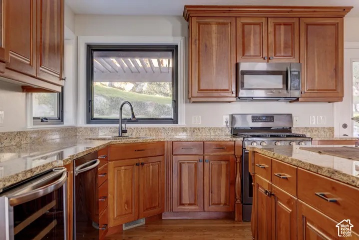 Wood-finish cabinetry, granite countertops, stainless steel appliances, corner sink with a gooseneck faucet, and a built-in beverage cooler