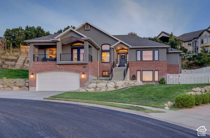Stucco and brick exterior with an arched garage door, upper-level balcony, and white picket fencing