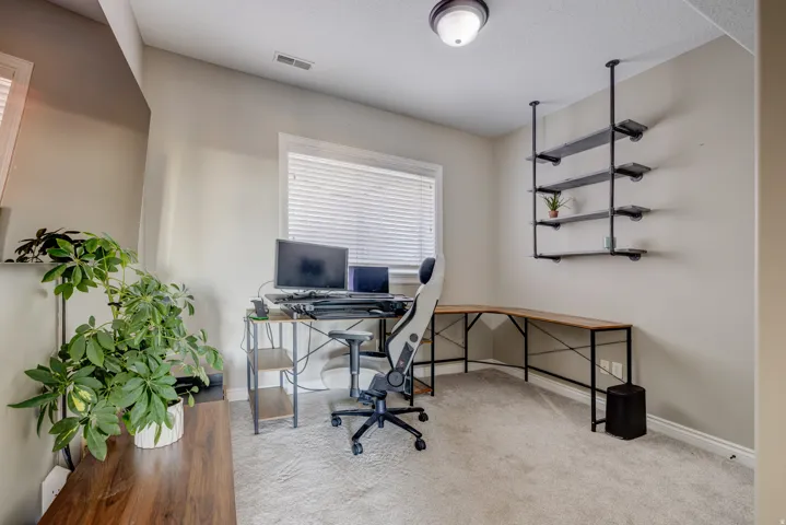 Neutral wall color, wall-mounted shelving unit, ceiling light fixture, wood-finish L-shaped desk