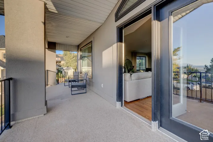 Covered balcony with a textured concrete surface, black metal railings, and a wood-finish ceiling
