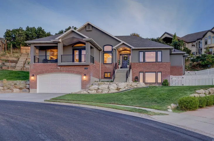 Stucco and brick exterior with an arched garage door, upper-level balcony, and white picket fencing
