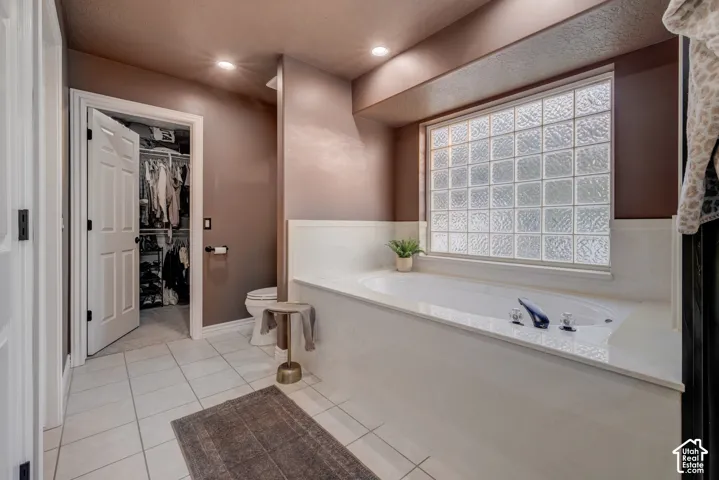 Built-in soaking tub with deck-mounted fixtures, glass block window, recessed lighting, and tile flooring