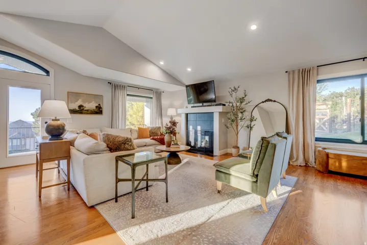 Vaulted ceiling with recessed lighting, wood-finish flooring, fireplace with a white mantel, large windows with drapery, and an arched transom window above a glass-paneled door