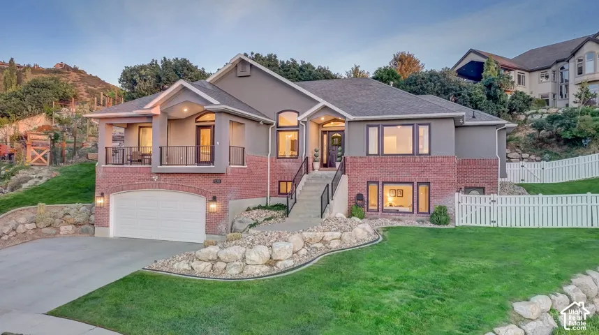 Multi-level residence featuring a brick and stucco exterior, an attached garage, and a covered balcony with a metal railing