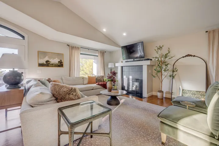Vaulted ceiling with recessed lighting, integrated fireplace with dark tile surround and white mantel, wood-finish flooring, and large windows