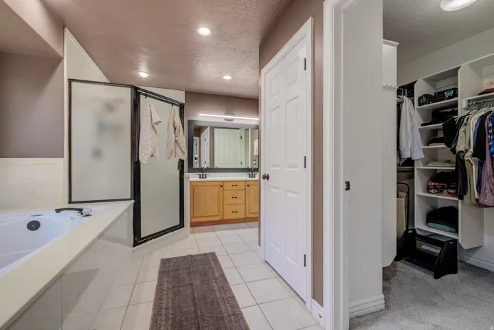 Recessed lighting illuminates the bathroom featuring a built-in tub, a glass-enclosed shower, and a dual-sink vanity with wood cabinetry